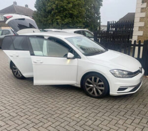Side view of a white estate car with doors and boot open on a driveway