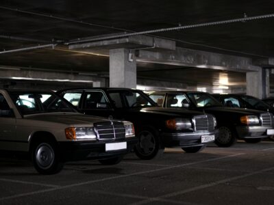 Three classic vintage Mercedes cars parked at night in underground parking garage with concrete pillars and structural beams overhead