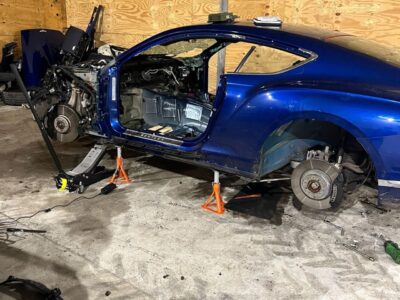 Dismantled blue Mercedes car with engine exposed, no wheels and safety cones in industrial workshop with yellow boarded walls and concrete floor