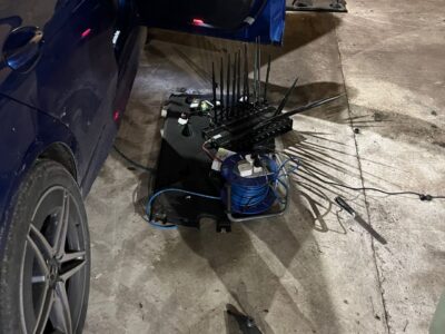 Stolen blue Mercedes with door open and engine parts and electrical components laid out on concrete workshop floor for forensic investigation