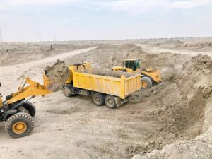 yellow wheel loader dumping soil into a dump truck at a quarry construction site