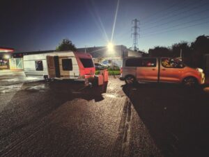 Orange stolen Toyota recovered vehicle parked at night in industrial recovery yard with caravans, facility lighting and power lines visible