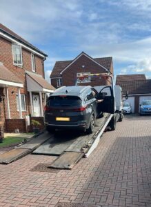 SUV being loaded onto a flatbed tow truck in a residential driveway